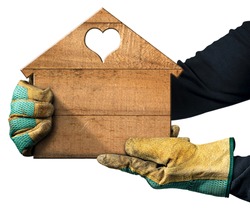 Closeup of two hands with protective work gloves holding a small wooden house with a heart-shaped hole. Isolated on white with copy space.