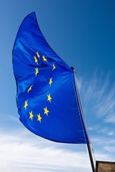 Close-up of an European Union flag waving against a clear blue sky with clouds and copy space.