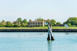 Abandoned and broken house in the Venice lagoon, and three big wooden poles implanted in the seabed called Briccola or Bricola (Dolphin), viable routes in the sea to boats. Veneto, Italy, Europe.