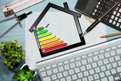 Energy efficiency rating graph on a desk with a house model, calculator, folding ruler, drawing compass, pencils and a computer keyboard