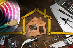 Home improvement concept - Wooden model house with folding ruler, work tools and a calculator on a wooden desk