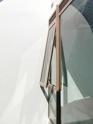 Wooden frame casement window ajar opened on white wall facade against daytime sunlight.