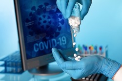 Doctor hand holds antiviral pills and background screen with illustration coronavirus covid-19 data. Researcher with oral pill bottle of pharmaceutical antiviral drugs against covid-19 coronavirus