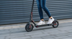 Close up of woman riding black electric kick scooter at cityscape, motion blur