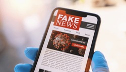 Online Corona Fake news on a mobile phone. Close up, man reading Fake news or articles about covid-19 in a smartphone screen application. Hand with gloves holding smart device. COVID19 nCov Outbreak.