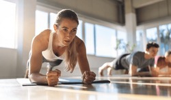 Fitness woman doing plank exercise workout in a group of people in gym. Sport girl and men in sportswear doing exercising on yoga mat, planking indoors