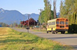 A morning rural school bus drives through a quiet country road in a beautiful agricultural valley. 