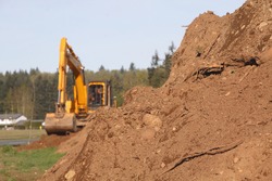 Soil or dirt in the foreground with an industrial shovel in the background/Heavy Lifters and Moving Earth/An industrial shovel a pile of dirt. 