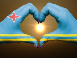 Gesture made by aruba flag colored hands showing symbol of heart and love during sunrise