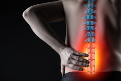 Pain in the spine, man with backache on black background, intervertebral hernia or disc injury concept