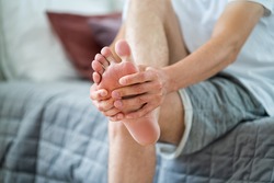 Foot pain, man suffering from feet ache in home interior, podiatry concept