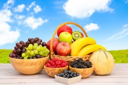 Group Healthy fresh fruit in a wooden basket, With vitamins c from bananas, kiwi, grapes, raspberries, blueberries, and blackberries, good for the body and diet food on the table in nature background.