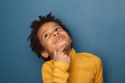 Small black child boy thinking and looking up on blue background