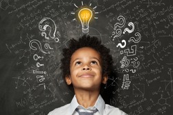Smart black kid with lightbulb. Brainstorming and idea concept. Little student boy on chalkboard background