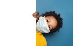 Black child boy in medical protective face mask holding white empty paper singbard