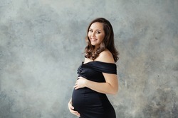 Fashion beauty portrait of happy pregnant woman in black dress on gray background