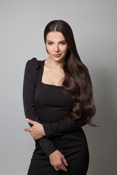 Fashion beauty portrait of a beautiful young brunette woman with long wavy hair wearing black cocktail dress posing
