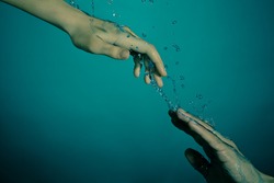 Underwater rescue concept. Female hand helping drowning male that going to dark sea floor.