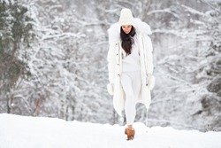 Beautiful Woman Wearing Fashionable Winter Clothes (white down jacket, knitted stylish hat, sweater, leggings, mittens, felt boots) Outdoors. Female stylish Model walking in winter nature