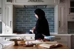 Arabian woman cooking in home kitchen, wears black abaya and hijab