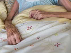 Skinny arms and hands of a very old woman lying in a bed