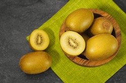 Kiwi gold yellow fruit in a wooden bowl with one sliced kiwi on grey table on background top view close up.