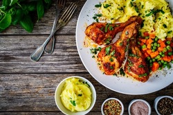 Barbecue chicken drumsticks with potato puree, grean peas and carrot on wooden table 