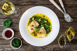 Fish dish - fried cod with spinach and capers in saffron sauce on wooden table 