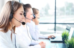 Portrait of smiling female customer service agent wearing headset with colleagues working in background at office.