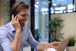 Smiling male business consultant with headphones sitting at modern office, video call looking at laptop screen. Man customer service support agent helpline talking online chat.