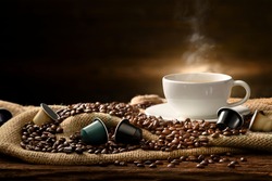 Cup of coffee with smoke and coffee beans and coffee capsules on burlap sack on old wooden background