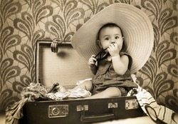 Baby girl sitting into the old suitcase retro image