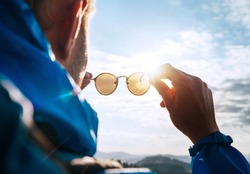 Backpacker man looking at bright sun through polarized sunglasses  enjoying mountain landscape. Eye  Vision Care human health concept image.