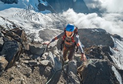 Climber in a safety helmet, harness with backpack ascending a rock wall with Bionnassay Glacier on background and looking at the summit during Mont Blanc ascending,France route.Active climbing concept
