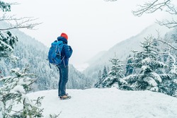 Female backpacker with backpack dressed warm down jacket enjoying snowy mountains landscape while she trekking winter mountain forest route. Active people in the nature concept image.