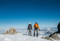 Couple connected team rope  with climbing harness dressed mountaineering clothes with backpacks and ice axes enjoying views ascending Mont Blanc (Monte Bianco) summit near Aiguille du Midi, France.
