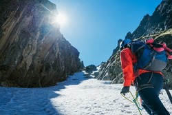 Team roping up woman dressed high altitude mountaineering clothes and harness climbing with backpack by snowy slope in the couloir with backlight sun on blue sky. Vysoke Tatry,Slovakia.