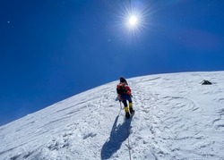Last steps before Kazbek (Kazbegi) summit 5054m rope team dressed mountaineering clothes, boots with crampons ascending by snowy slope with blue sky background and bright sun. East Caucasus mountains.