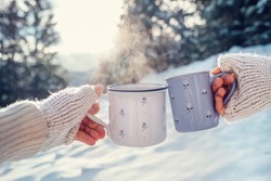 Man and woman hands in knitting mittens with cups of hot tea on winter forest glade