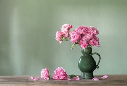 pink peonies in ceramic jug on green background