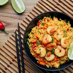 Quick and healthy Asian meal made of fried rice, fresh shrimps, lime and vegetables in a black bowl on a wooden table. Top view, directly above shot.