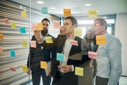 Group of business people brainstorming with sticky notes on glass window