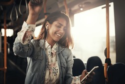 Young woman smiling while standing by herself on a bus listening to music on a smartphone 
