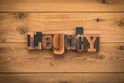 Legacy, single word written with vintage letterpress printing blocks on rustic wood background.