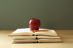 apple on stack of open books with pencil 