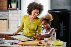 Mother Teaching Child to Cook and Help in the Kitchen. African American Mother and Daughter making cookies at home. 