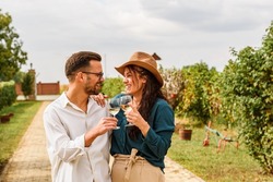 Young smiling couple tasting wine at winery vineyard - Friendship and love concept with young people enjoying harvest time 