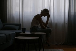 Young depressed woman sitting on the sofa next to the window	