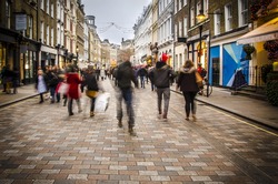Shoppers walking down busy retail high street in London. Motion blurred 