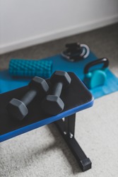 home gym and fit lifestyle still-life, room with flat bencha nd dummbells surrounded by other fitness equipment like yoga mat with kettlebell and jumping rope shot at shallow depth of field
